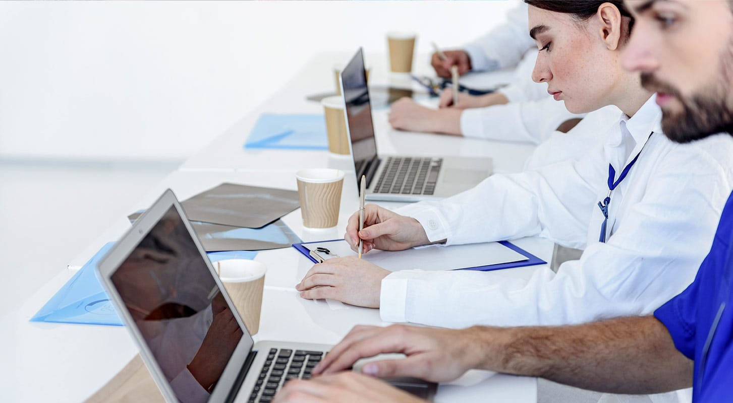 Doctors seated at a table, using laptops to discuss patient care and share information.